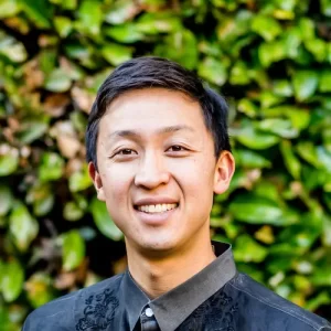 Eric Tuan, composer, in front of a green hedge background