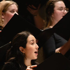 3 Seattle Choral Company sopranos singing, with black concert folders